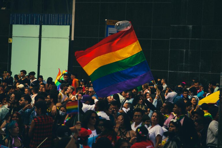 A lively crowd celebrating at a Pride parade with vibrant rainbow flags.