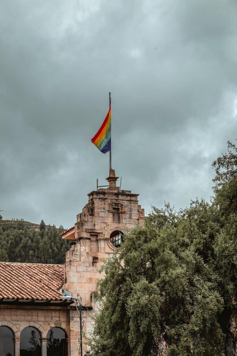 A stone building with a rainbow flag in Cusco, Peru under cloudy skies.