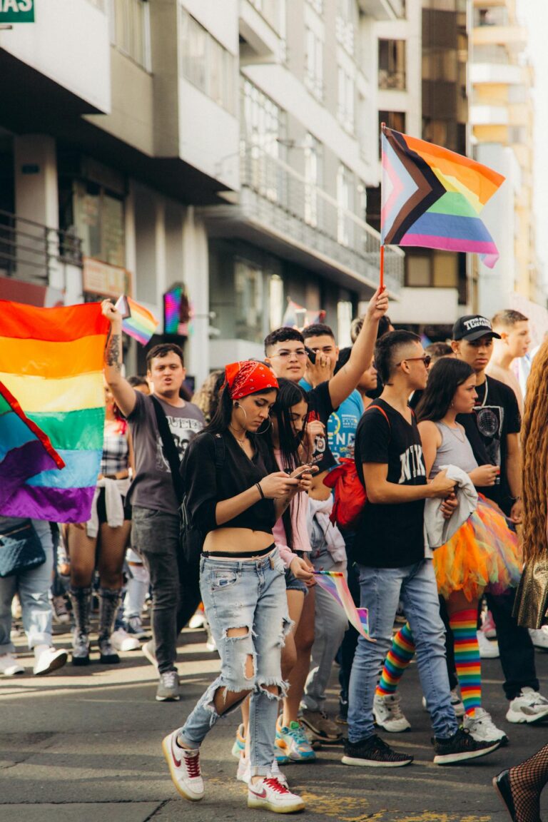 Vibrant LGBTQ+ pride parade with diverse crowd waving rainbow flags outdoors during the day.